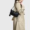 A woman is holding a beige trench coat and a black leather tote bag with a gold metal buckle.