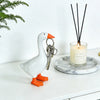 A white resin goose sculpture with orange feet and a key holder resting on a marble coaster next to a candle.