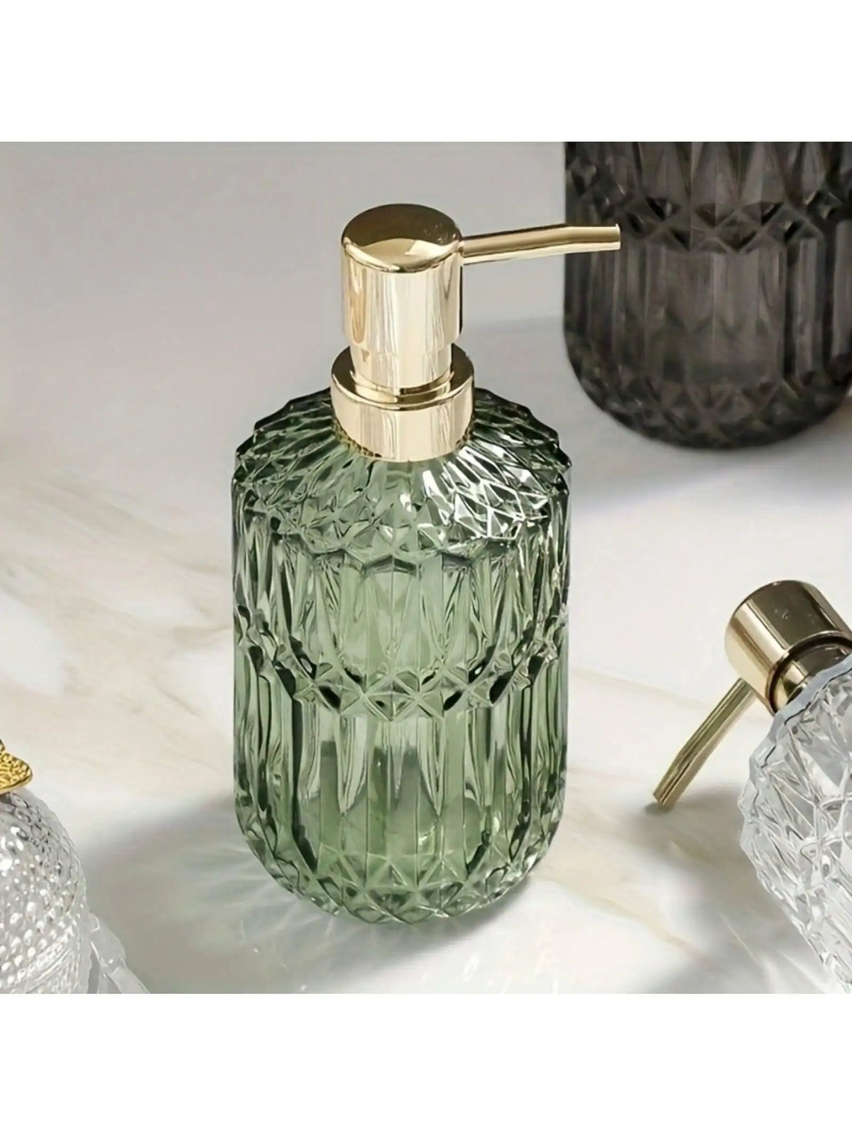 A clear green glass bottle with a gold pump dispenser sits on a white marble surface.