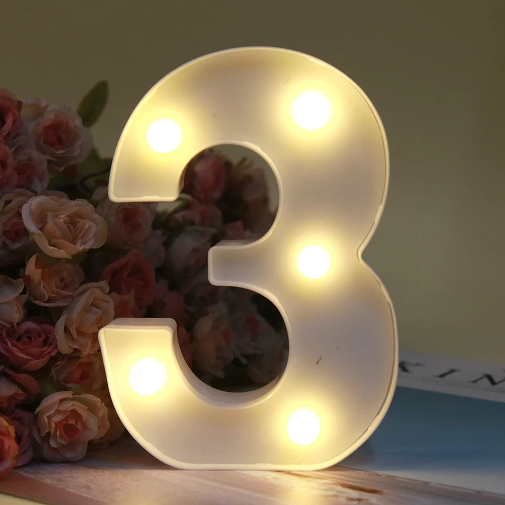 Lumière de nuit alphabet LED blanche brillante en forme du chiffre trois posée sur une surface en bois à côté de roses roses.