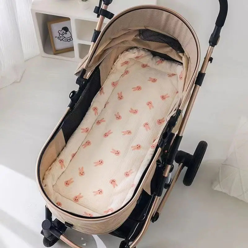 A beige baby stroller seat cushion with pink embroidered bunnies and padded support is shown on a light-colored floor.