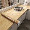A wooden roll of self-adhesive wallpaper is placed on a kitchen countertop next to a window view.