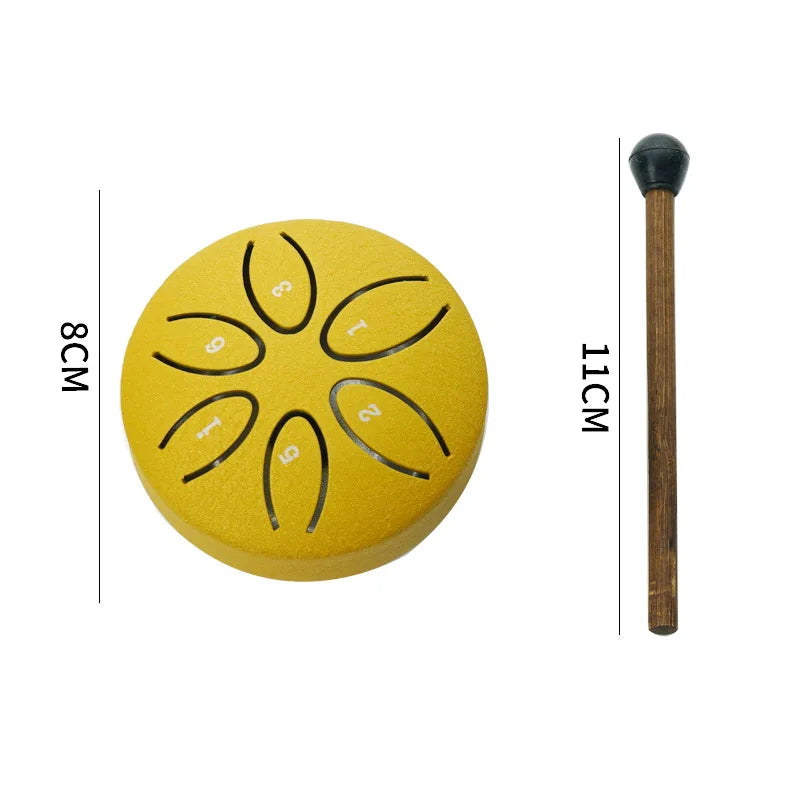 A yellow mini steel tongue drum with six tuning holes and a wooden mallet shown next to a measurement scale.