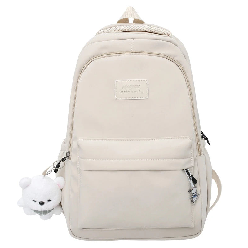 A beige waterproof nylon laptop backpack with a white bear charm attached to the zipper.
