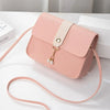 A light pink compact crossbody handbag with a beige strap and gold-toned charm resting on a white surface.