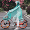 A person wearing a transparent, iridescent waterproof poncho with a hood rides an orange bicycle on a paved road.