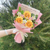 Sträußchen aus handgefertigtem Häkelblumenmuster in Gelb und Pink, in rosa Papier eingewickelt