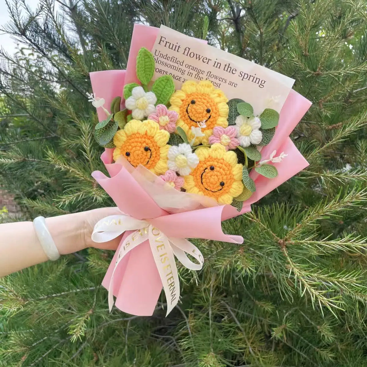 Sträußchen aus handgefertigtem Häkelblumenmuster in Gelb und Pink, in rosa Papier eingewickelt