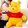 A yellow Winnie the Pooh plush toy sitting on a light-colored sofa, next to a person holding a camera.