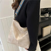A beige vintage bohemian shoulder bag with blue embroidery is shown hanging from a dark blazer sleeve.