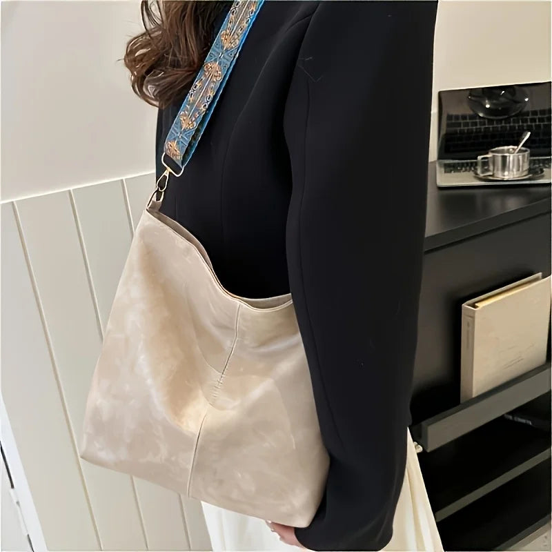 A beige vintage bohemian shoulder bag with blue embroidery is shown hanging from a dark blazer sleeve.