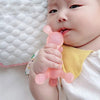 A baby is holding a pink silicone cartoon rabbit teether with its mouth, resting on a white surface.