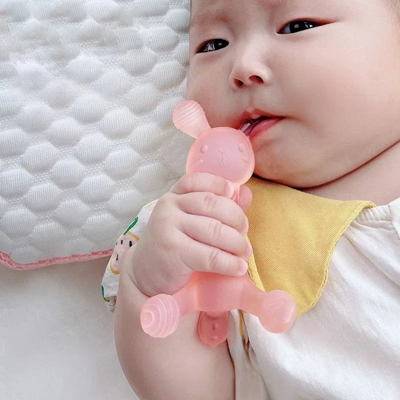 A baby is holding a pink silicone cartoon rabbit teether with its mouth, resting on a white surface.