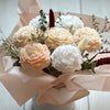A bouquet of soft peach and white peony-like flowers arranged in pink tissue paper.