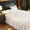 White quilted bed skirt with gold trim and white pillows on a dark headboard