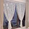 Rideaux transparents avec broderie florale blanche, suspendus à une fenêtre avec des draperies neutres.