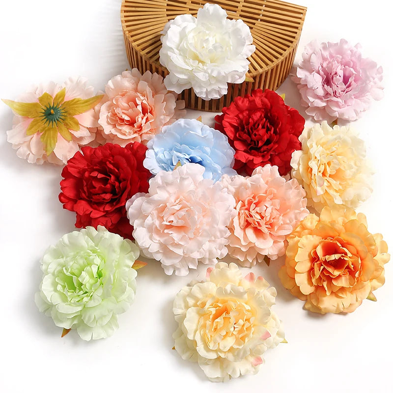A collection of silk peony flower heads in various shades of pink, orange, red, and white arranged on a wooden mat.