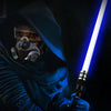A person wearing a dark hooded cloak is holding a glowing blue lightsaber in a dark environment.