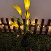 A vertical arrangement of yellow calla lily flowers illuminated by solar-powered LED lights in a garden setting.