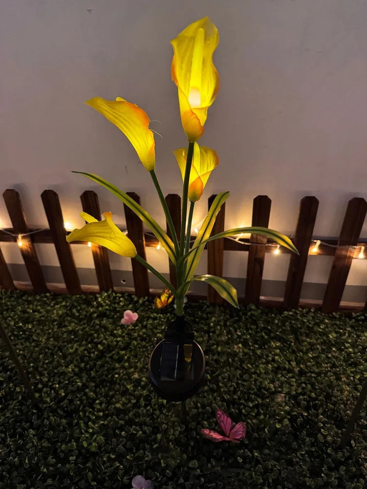 A vertical arrangement of yellow calla lily flowers illuminated by solar-powered LED lights in a garden setting.