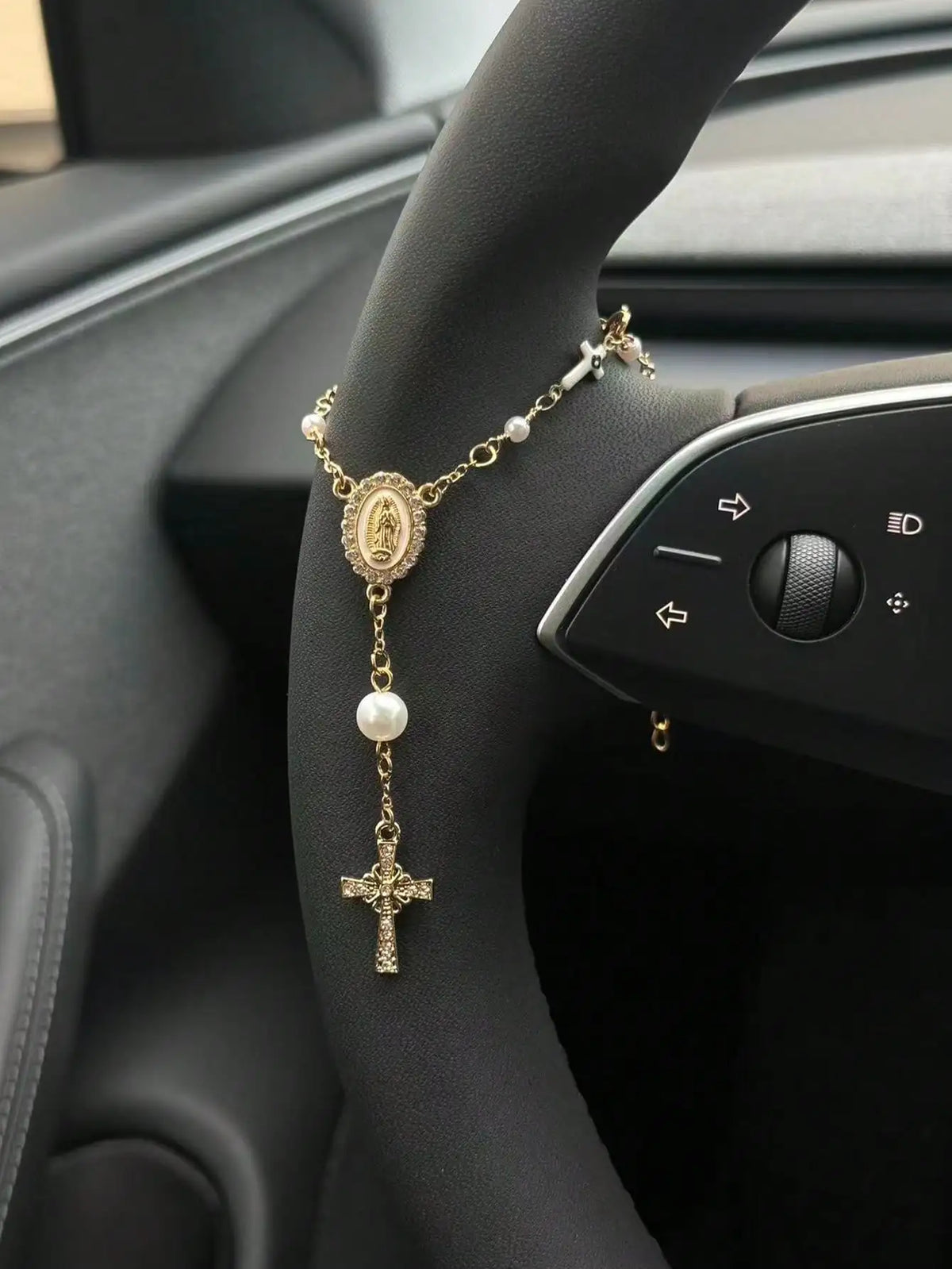 A gold-colored rosary necklace with a crucifix and pearl beads is displayed on a person's wrist.