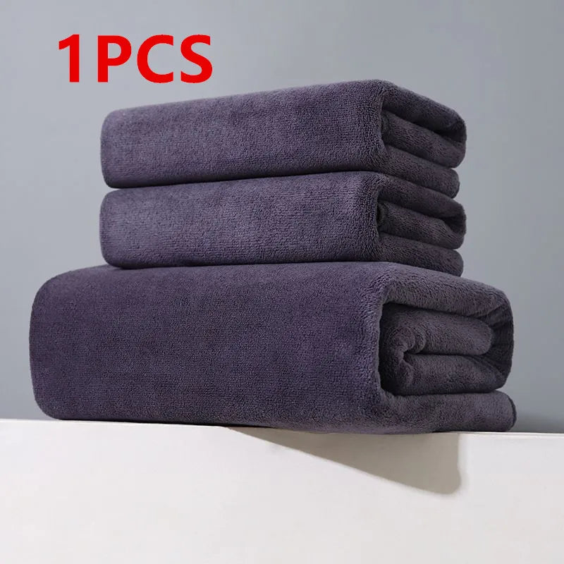 A stack of three dark gray microfiber bath towels on a white surface.