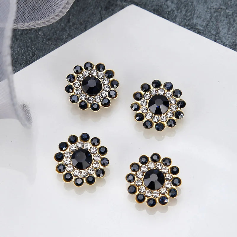 A set of five gold-toned flower rhinestone embellishments with dark blue and clear stones on a white surface.
