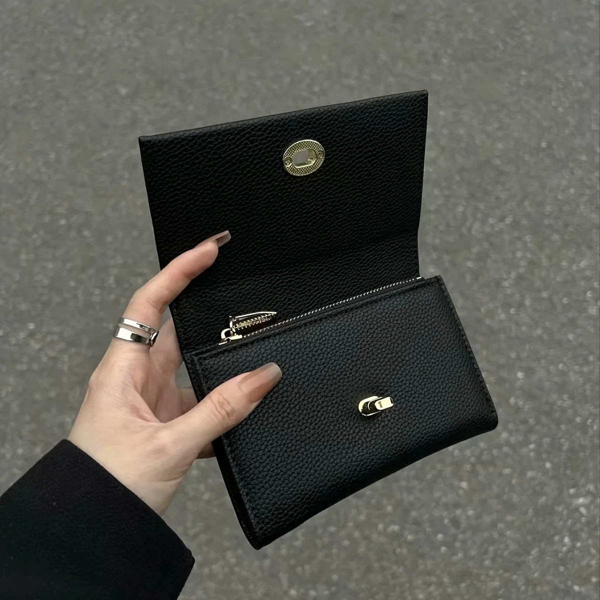A hand holds open a sleek black compact wallet with gold accents against a gray background.