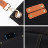 Close-up view of a brown leather strap and brass hardware attached to a black canvas fabric, showing stitching details.