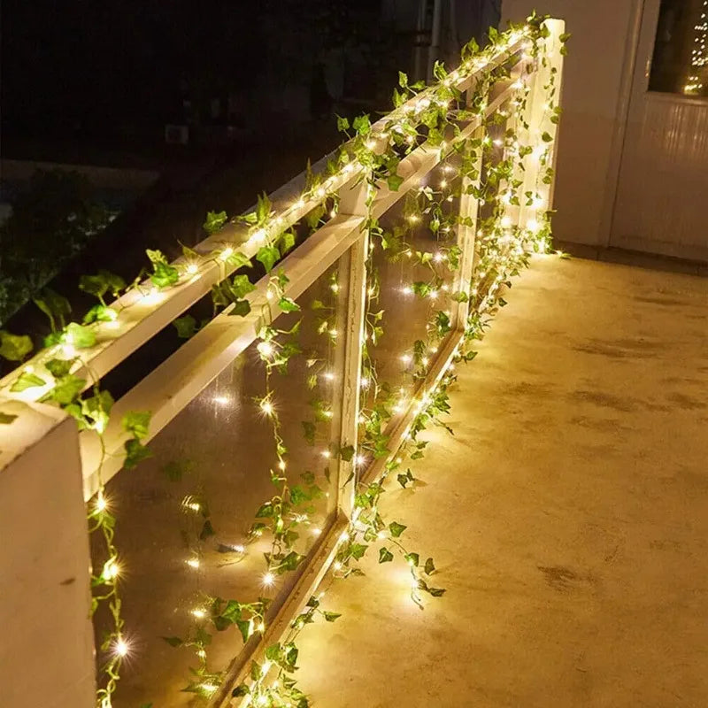 Une clôture en bois décorée de guirlandes de lierre LED lumineuses illuminant la structure la nuit.