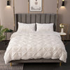 A white 3D pinch pleated duvet cover set displayed on a bed with a gray upholstered headboard.