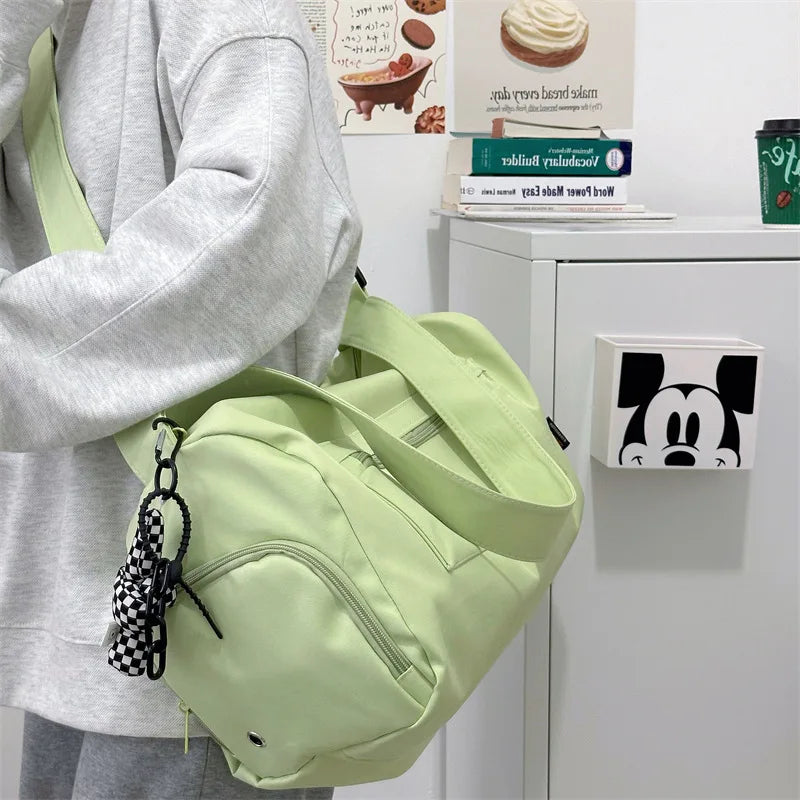 A light green canvas travel tote bag with a black patterned crossbody strap is shown next to a white Mickey Mouse framed pict