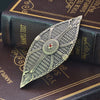 A detailed metal sword ornament with intricate feather patterns rests on a dark leather-bound book.