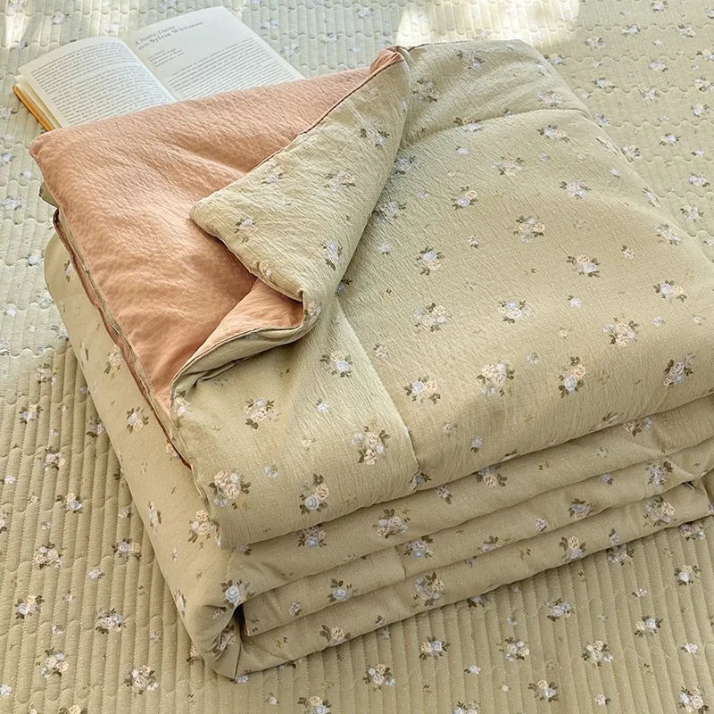 A stack of light beige and peach patterned quilts resting on a textured fabric surface.