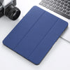 A dark blue Retro Marble iPad Pro case with a built-in pencil holder resting on a white surface next to a laptop and camera.