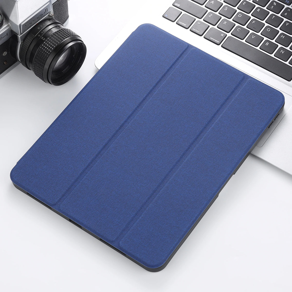 A dark blue Retro Marble iPad Pro case with a built-in pencil holder resting on a white surface next to a laptop and camera.