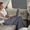 A woman sits in a car, using a laptop while the magnetic car window sunshades are partially deployed.