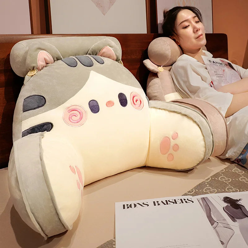 A light gray plush cat and dog backrest cushion is shown resting on a brown sofa, with a woman nearby.