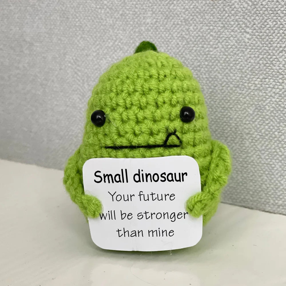 A handmade green crochet dinosaur doll with a sad expression and a note that says Your future will be stronger than mine