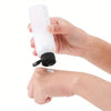 A hand is holding a white refillable travel bottle with a flip cap.