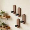 A set of three vertical walnut wood hooks mounted on a light wall for entryway or bathroom organization.