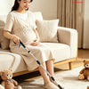 A pregnant woman sits on a sofa holding a foldable grabber tool with a magnetic swivel head.