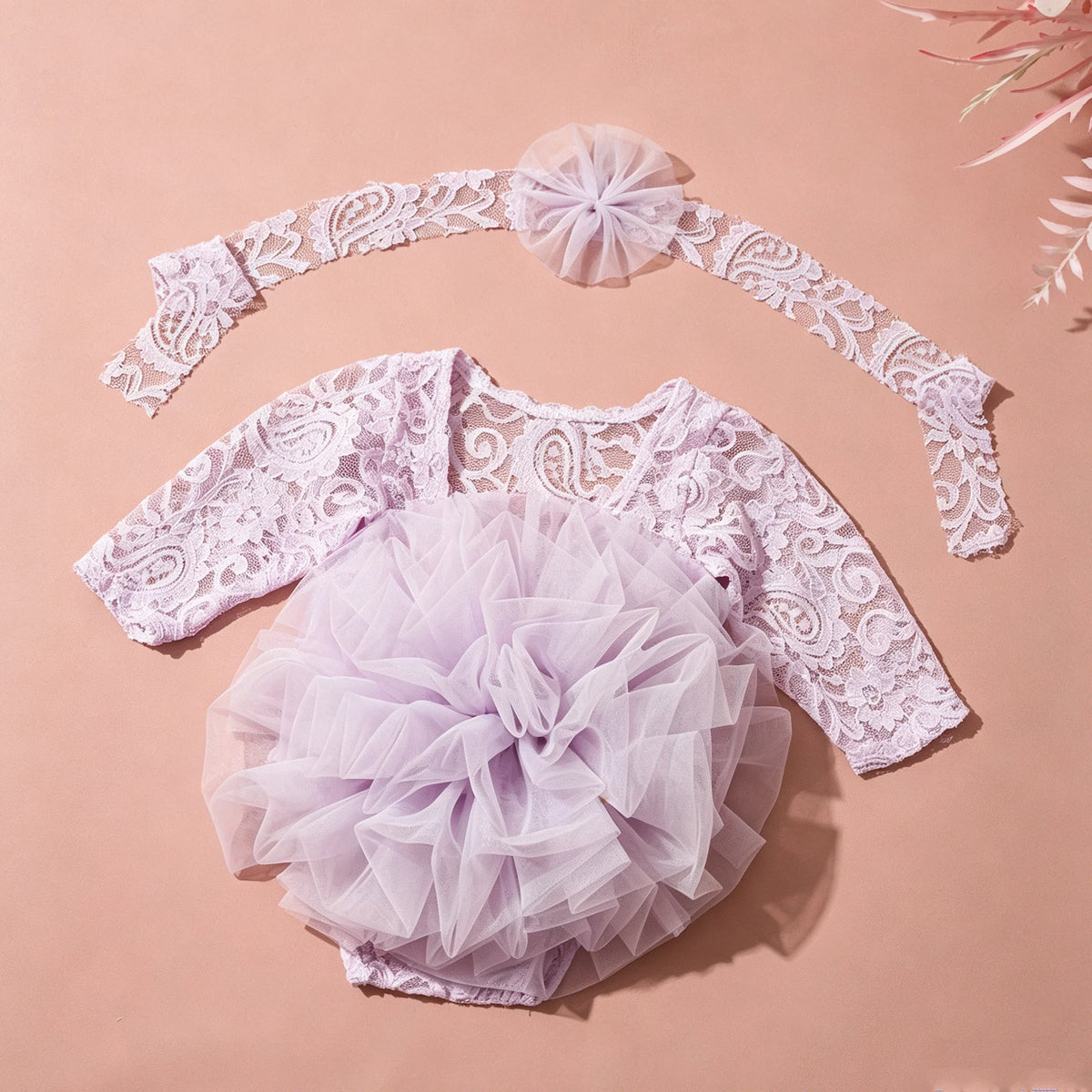 A light purple lace romper dress with a ruffled tutu skirt and matching headband laid on a pink background.