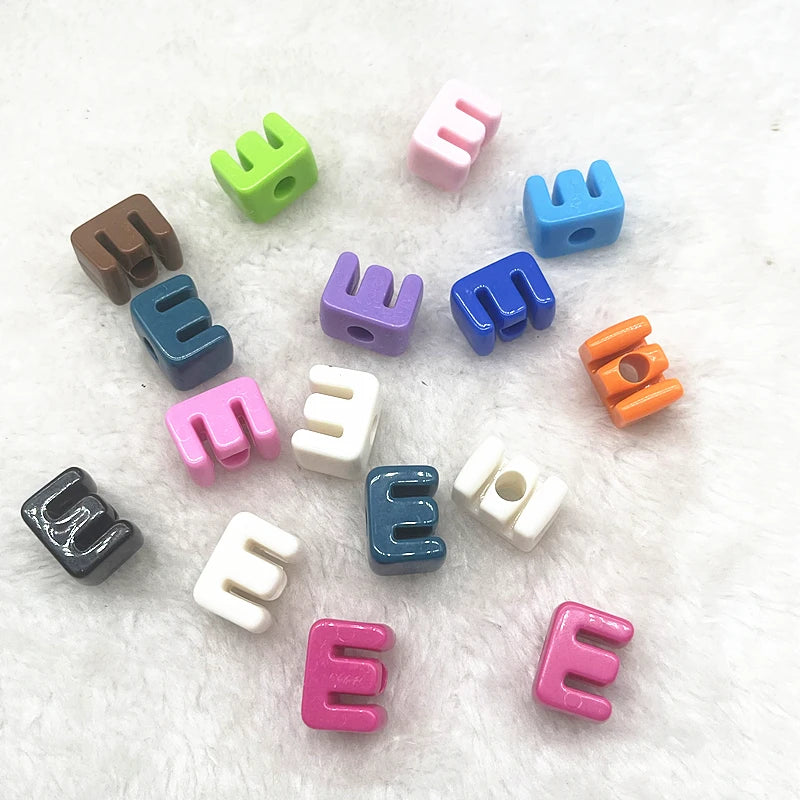 A collection of ten mixed alphabet letter beads in various colors and shapes scattered on a white surface.