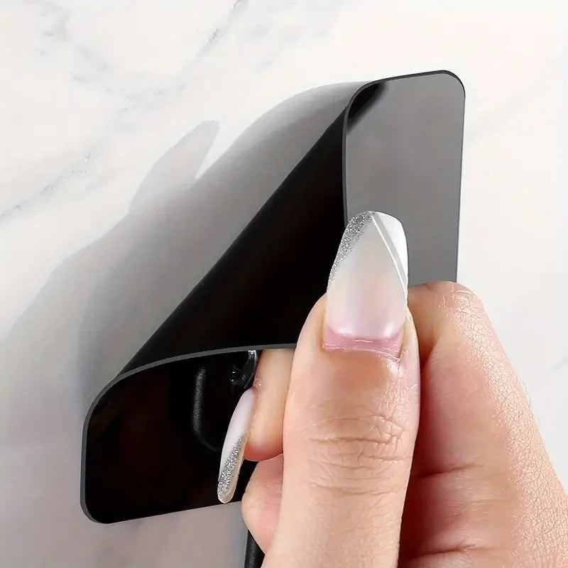 A hand is holding a black adhesive hook with a clear, glittery tip against a white marble background.