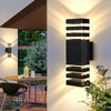 A modern black LED wall sconce with vertical light strips illuminates a white wall outdoors.