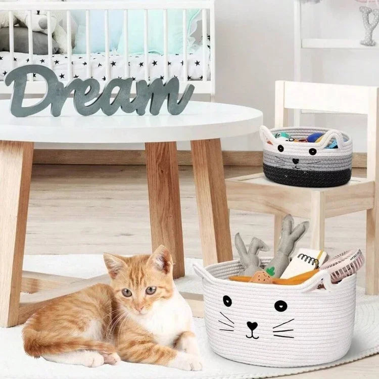 A small orange and white kitten is resting next to a white woven cotton rope storage basket with handles.