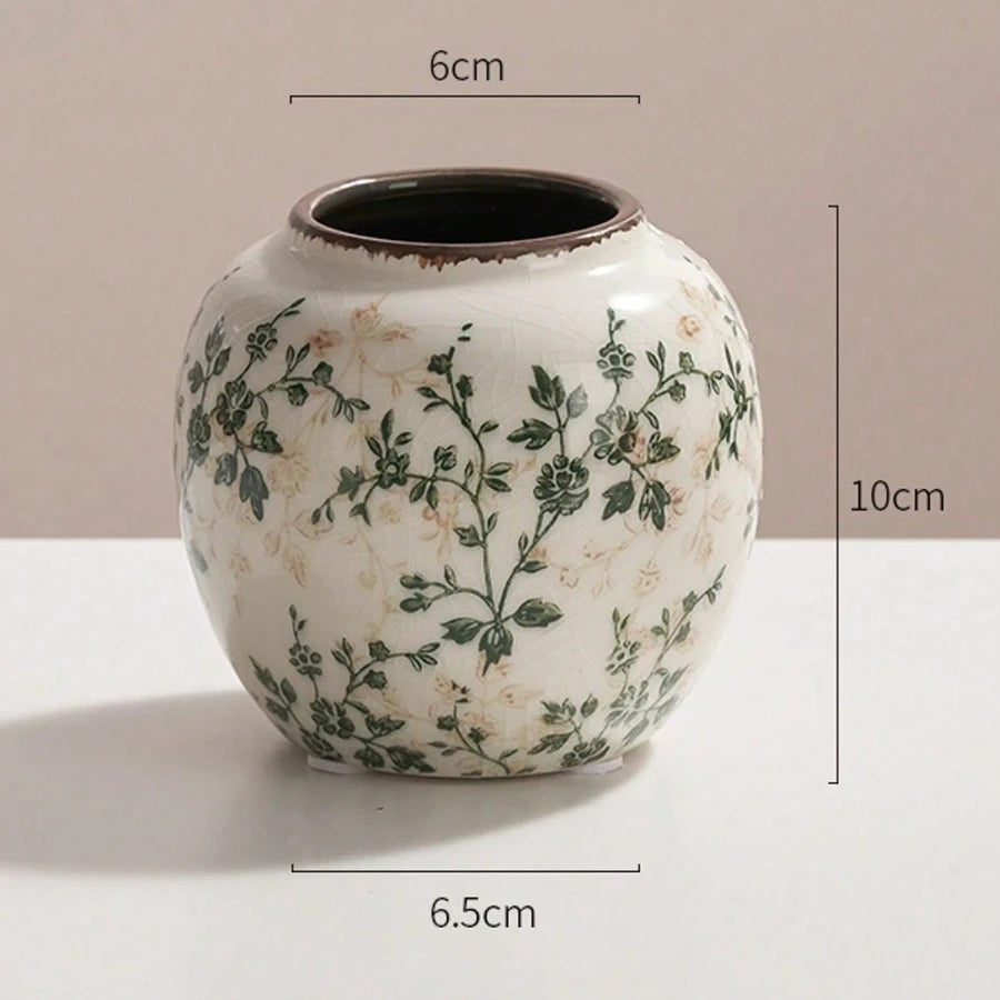 Weiße Keramikvase mit grünen Blumenmustern und dunklem Rand, vor hellem Hintergrund.