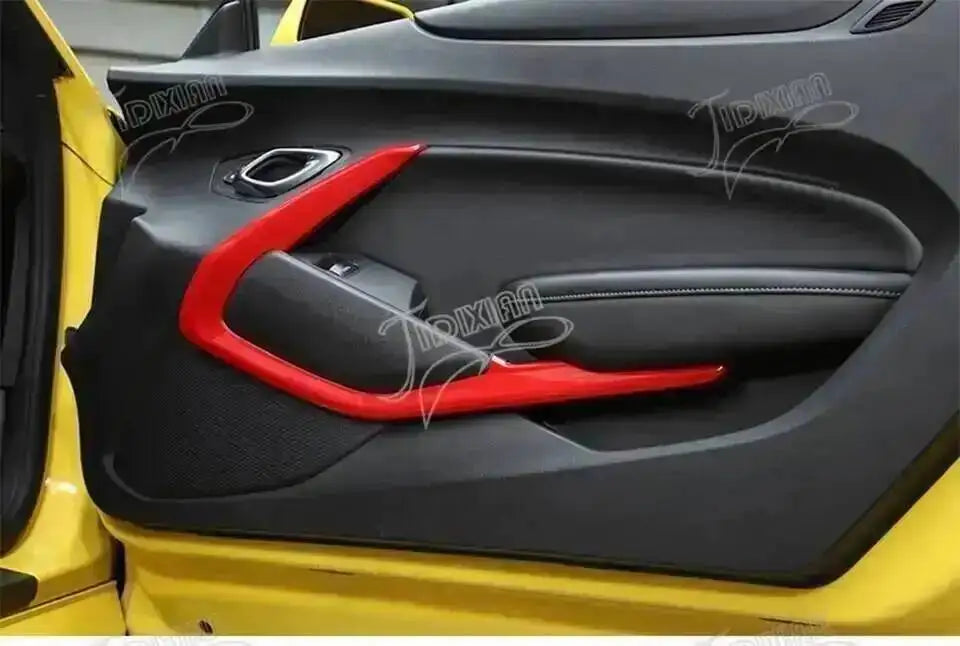 Close-up of a red interior trim piece installed in the black plastic panel of a yellow Chevrolet Camaro.