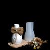 A white silicone mold for candle and vase projects is displayed next to dried floral elements on a wooden surface.